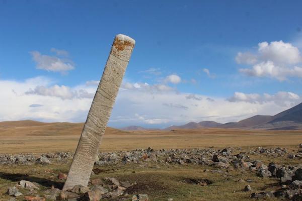 Une  pierre de cerf   penchée placée devant des douzaines de petits monticules de pierre contenant des sépultures de chevaux sacrifiés rituellement sur le site du monument de l’âge du bronze d’Ikh Tsagaanii Am, dans la province de Bayankhongor, en Mongolie centrale. (Image : William Taylor)